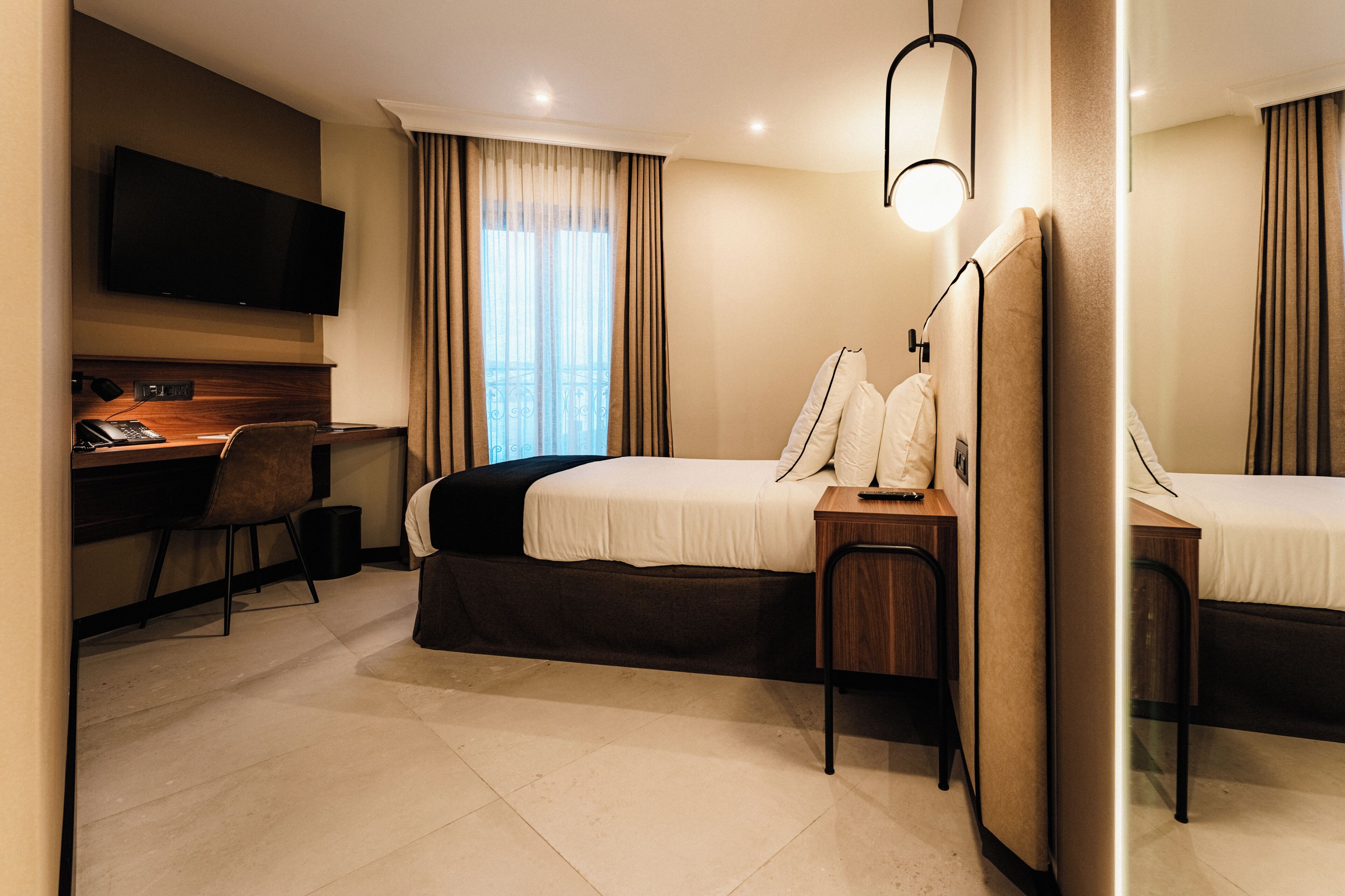 A hotel room with a bed, a desk, a chair, a TV, and a window with curtains.