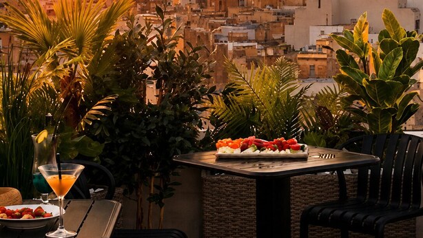 Eine Terrasse mit Sonnenuntergangsblick, ein Tisch mit einer Obstplatte und ein Martini-Glas.