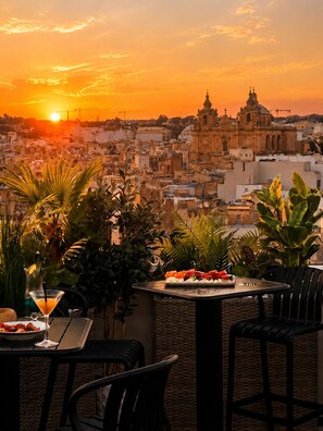 A terrace with a sunset view, a table with a fruit platter, and a martini glass. - Royale Sainte Hélène Boutique Hotel (Birkirkara)