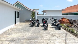 Un patio empedrado con tres motocicletas estacionadas en fila, un árbol pequeño y una pila de ladrillos.