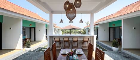 A dining area with a wooden table set for four, surrounded by wicker chairs, under a ceiling with hanging light fixtures.