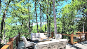 Une terrasse en bois, agréée de mobilier d’extérieur, entourée d’arbres et offrant une vue sur un ciel dégagé.