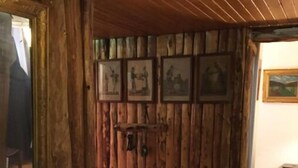 A rustic room with wooden walls, a wooden dresser, and a mirror. There are framed pictures on the wall and a small table with a rug.