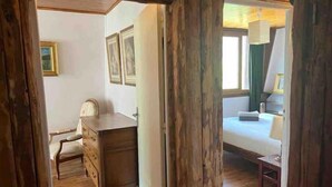 A room with a wooden desk, a bed, and a chair. There are framed pictures on the wall.