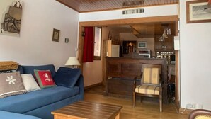 A living room with a blue sofa, a wooden coffee table, and a wooden-framed door leading to a kitchen.