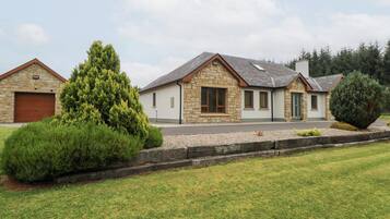 Une maison en pierre à deux étages, dotée d’un garage, d’une pelouse bien entretenue et d’un grand conifère dans le jardin.
