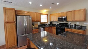 A modern kitchen with wooden cabinets, stainless steel appliances, granite countertops, and recessed ceiling lights.