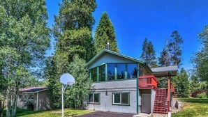 A two-story house with a green roof, a covered porch, and a basketball hoop in the driveway.