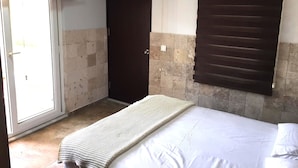 Um quarto pequeno e estreito com uma cama, uma porta e uma janela com persianas.
