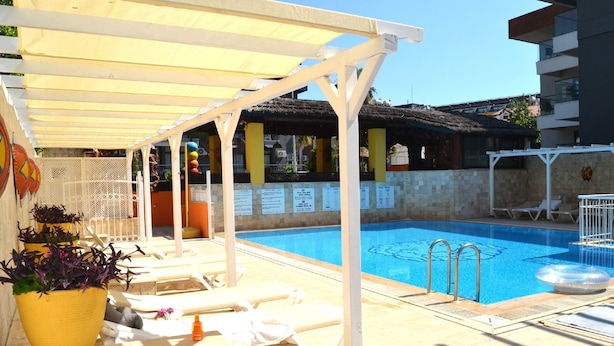 Uma área de piscina com espaço de estar coberto, cadeiras de espreguiçadeira e um vaso de planta.
