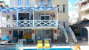 Um hotel com vários andares, com área de piscina, incluindo terraço solar com cadeiras amarelas e área de estar coberta.