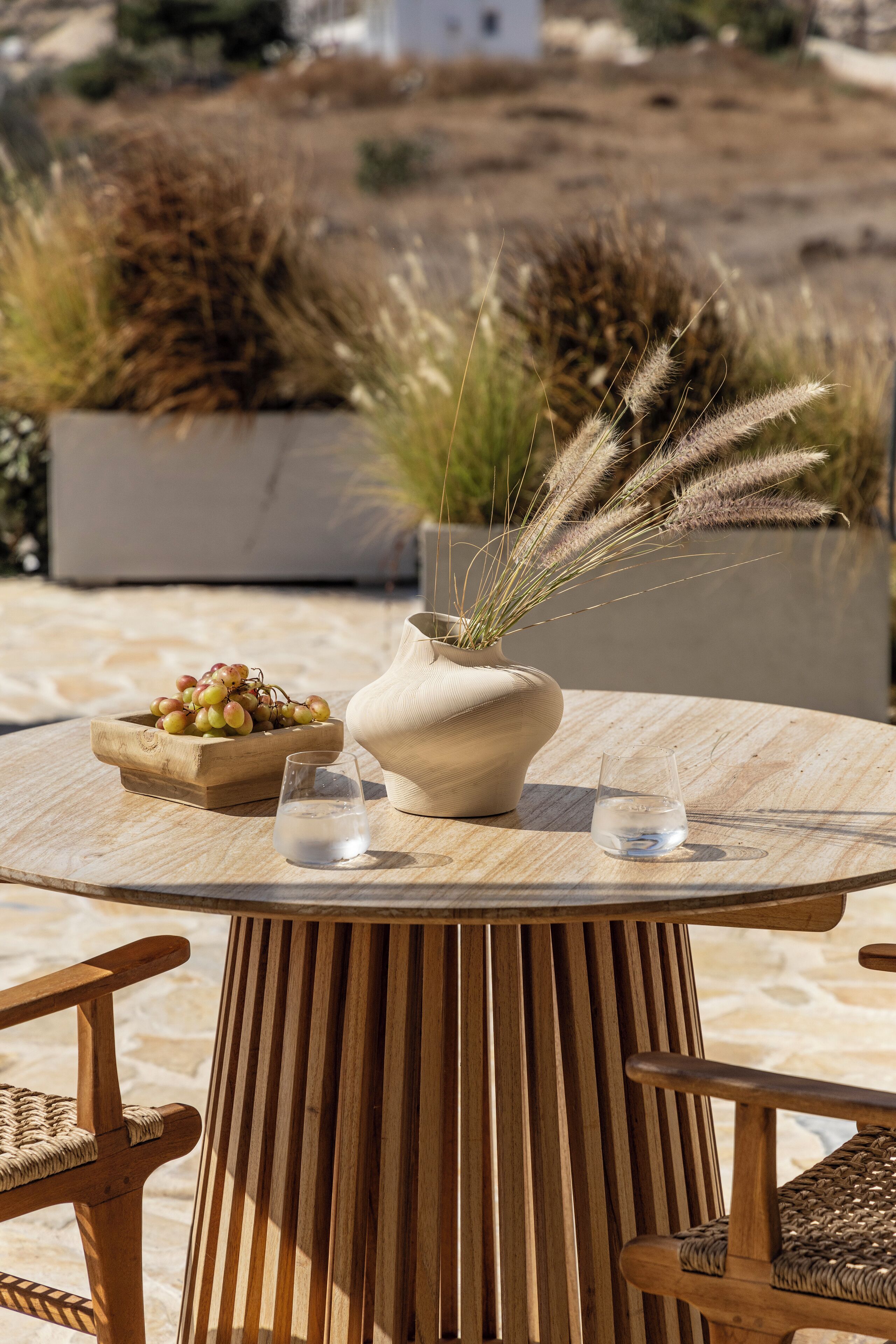 Une table ronde en bois, sur laquelle se trouvent un vase, un bol de raisins et deux verres d’eau.