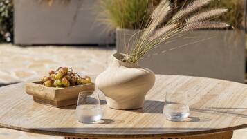 A round wooden table with a vase, a bowl of grapes, and two glasses of water.