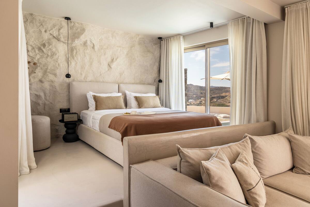A modern bedroom with a large bed, a sofa, and a view of the outdoors.