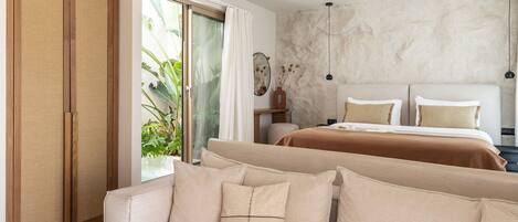 Una habitación de hotel moderna con sofá, cama con dos almohadas, mesita de noche y una ventana grande con cortinas.