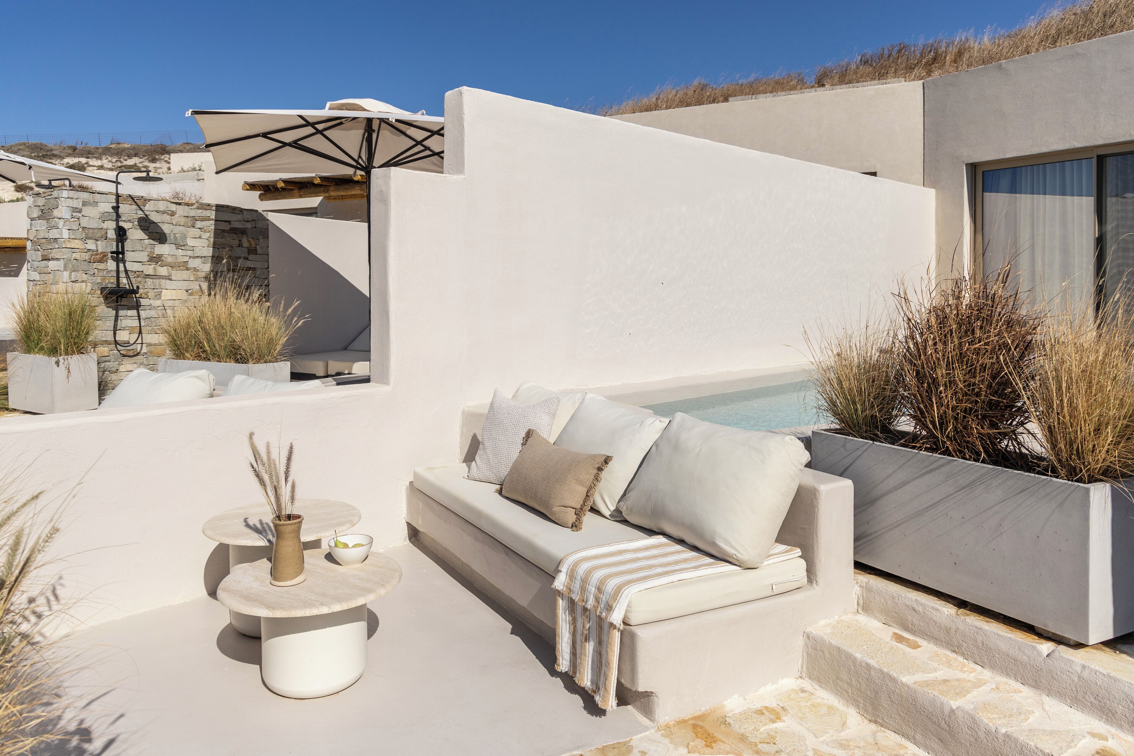 Un espacio moderno al aire libre con sofás, dos mesas redondas y una jardinera con plantas.