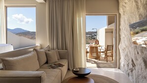 A modern living room with a sofa, a coffee table, and a view of the outdoors through a large window. - Solus Suites (Milos)
