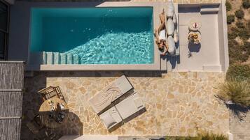 An aerial view of a rooftop pool area with a stone wall, lounge chairs, and a table with food and drinks.