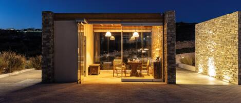 A modern outdoor dining area with a glass enclosure, stone walls, and ambient lighting.