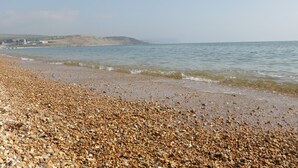 A pebble beach with calm water and a distant view of hills. - Mellstock (Weymouth)