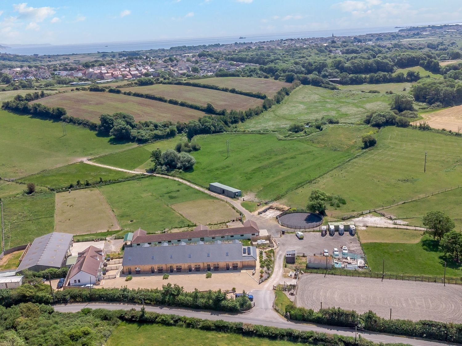 An aerial view of a rural property with a large barn, open fields, and a small residential area in the background.
