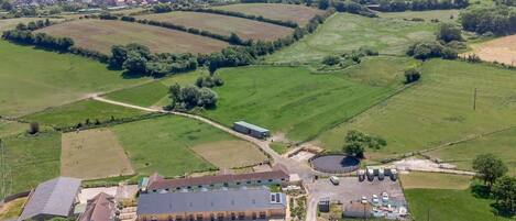 An aerial view of a rural property with a large barn, open fields, and a small residential area in the background.