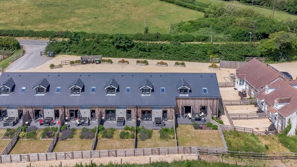 A large building with multiple rooms, a covered outdoor area with seating, and a fenced-in horse riding area. - Mellstock (Weymouth)