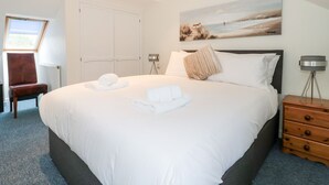A neatly made bed with white linens and towels, a painting of a beach scene, and a wooden nightstand with drawers. - Mellstock (Weymouth)