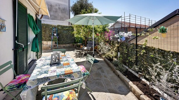 A patio with a table set for two, a green umbrella, and a stone pathway. - Cod Citra 008031-lt-1216 Affitto Pittoresca Casina Indipendente con Giardino (Imperia)