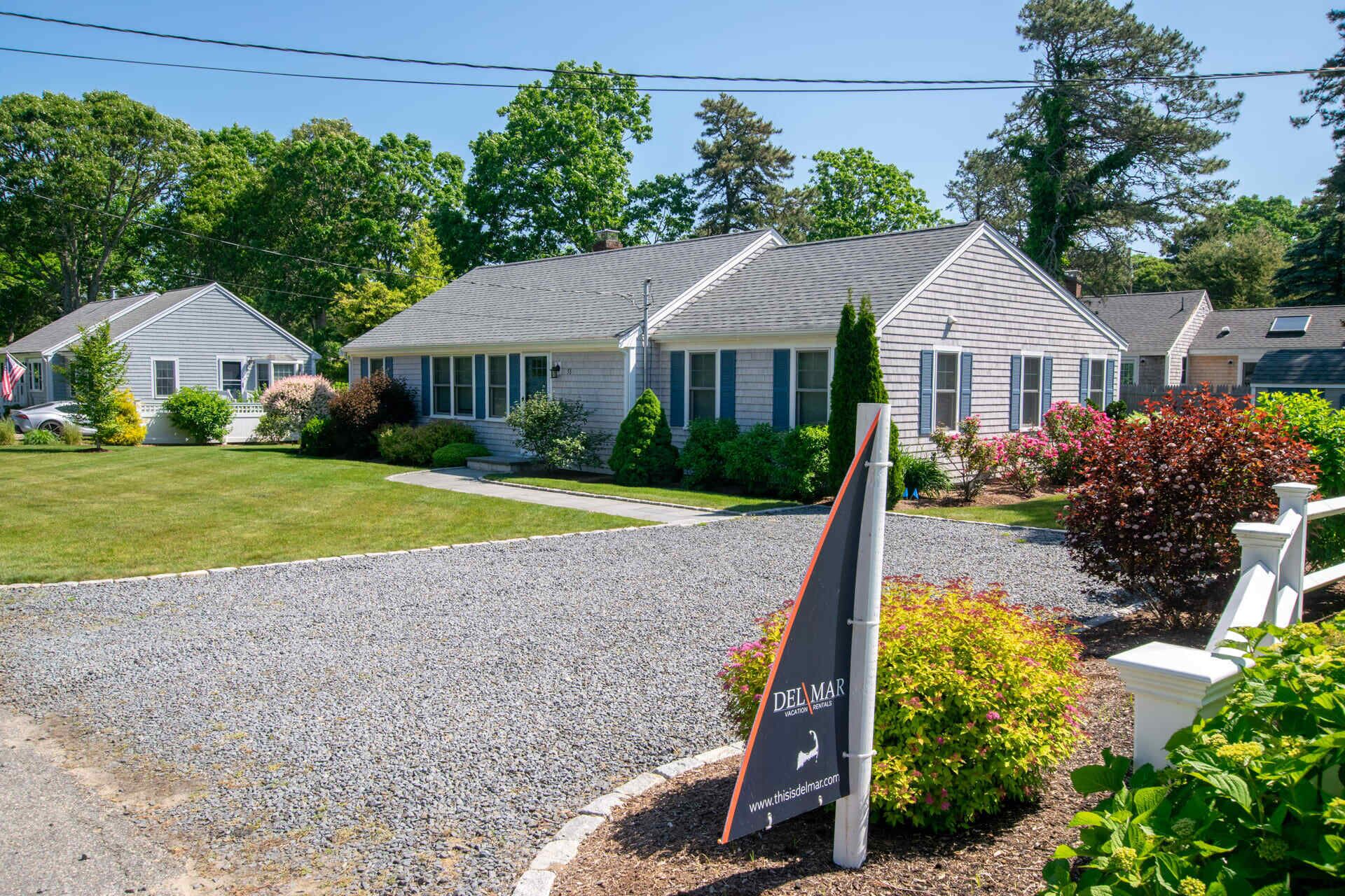 A row of single-story houses with a gravel driveway and a sign for Delmar Vacation Rentals.