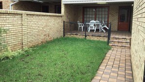 Una casa de ladrillo con un pequeño jardín, un patio con sillas y una puerta.