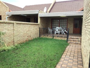 A brick house with a small lawn, a patio with chairs, and a door. - Cozy 2BR 2BR Townhouse Netflix Private Parking Great Location! (Bloemfontein)