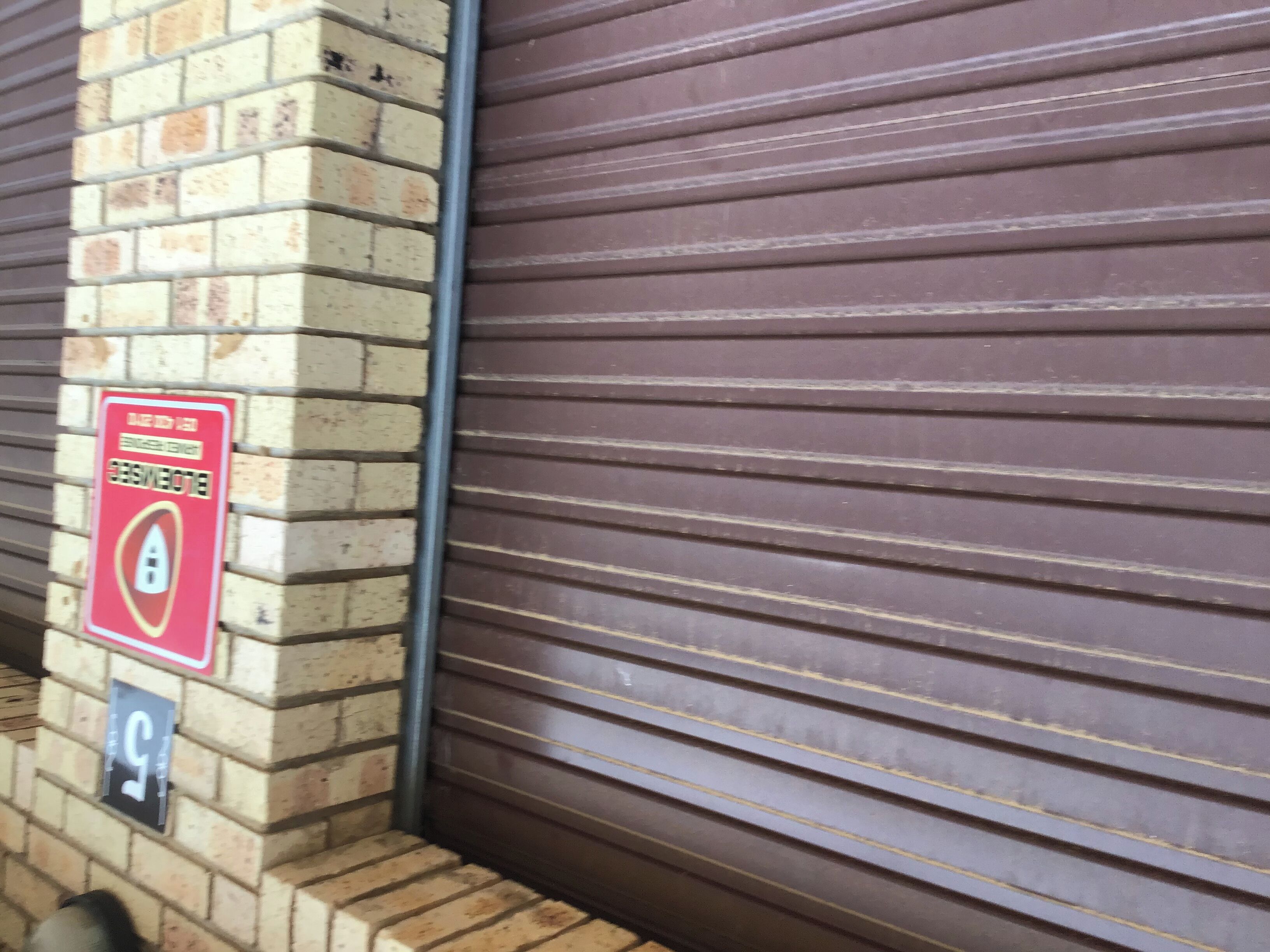 Un mur de briques avec un volet métallique fermé et un panneau rouge indiquant une zone où l’éclairage est coupé.