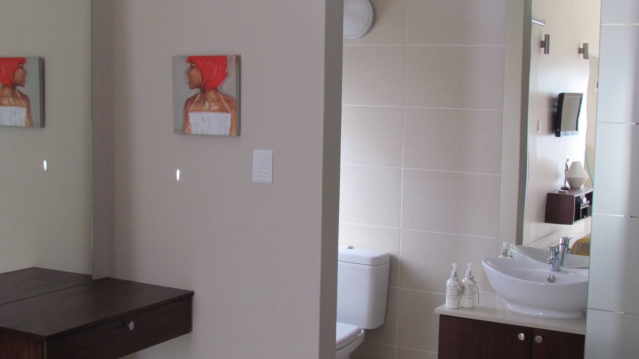Un bagno con il water, un lavandino, uno specchio e due quadri appesi al muro.
