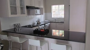 A kitchen with a black countertop, white cabinets, a microwave, a sink, and a window with blinds. - Comfortable Furnished Apartment Wi-fi Free Parking (Bloemfontein)