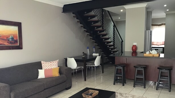 A modern living room with a grey sofa, a black coffee table, and a staircase leading to a kitchen area. - Furnished Apartment Long Or Short Bloemfontein (Bloemfontein)