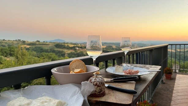 A table set with bread, cheese, and cured meat on a balcony with a scenic view.