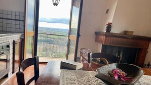 A dining area with a view of a mountainous landscape through open doors, a fireplace, and a kitchen with a tiled backsplash.