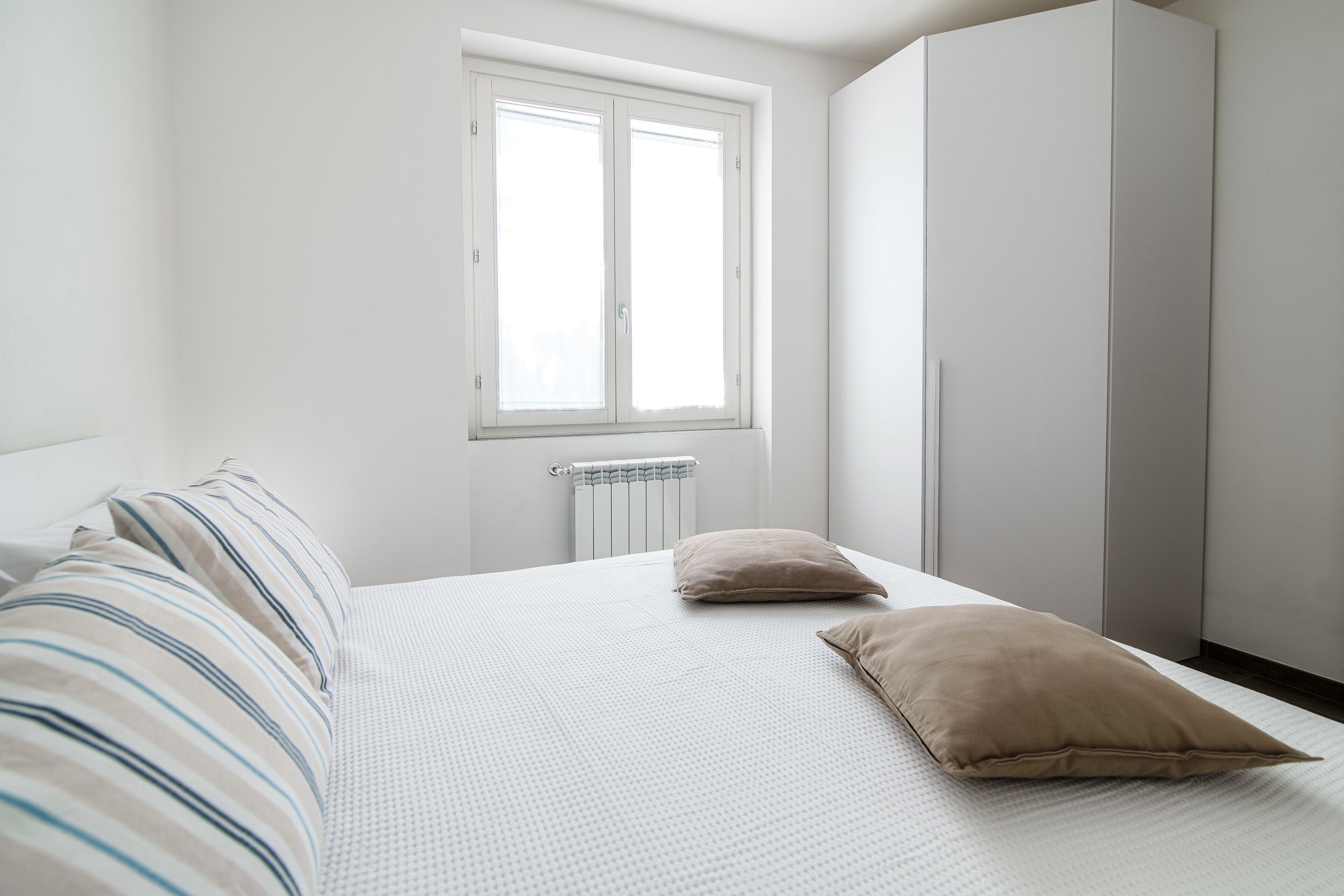 Un dormitorio con cama, dos almohadas, un radiador y una ventana.