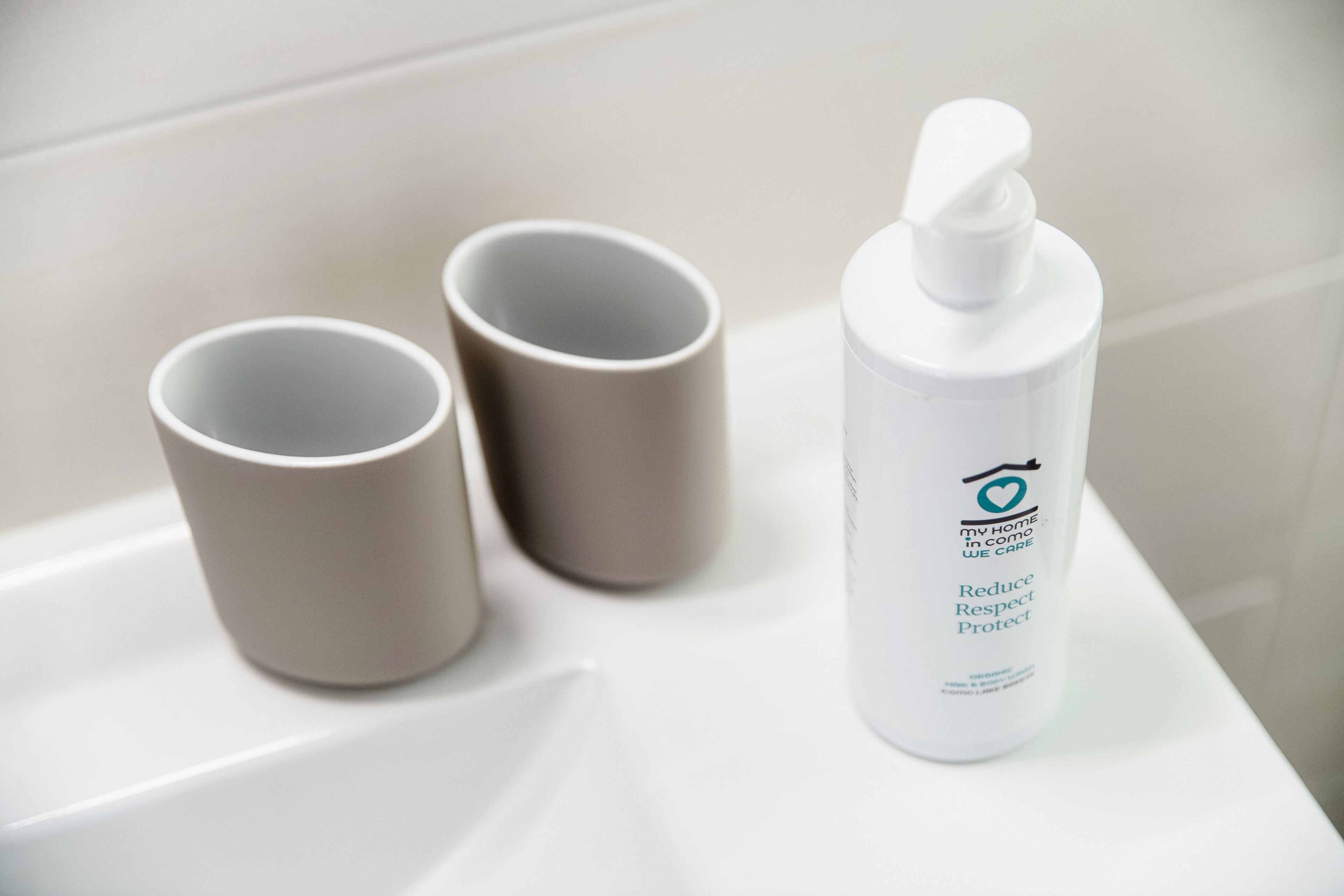 A bathroom with a white sink, two beige cups, and a white bottle of hand soap.