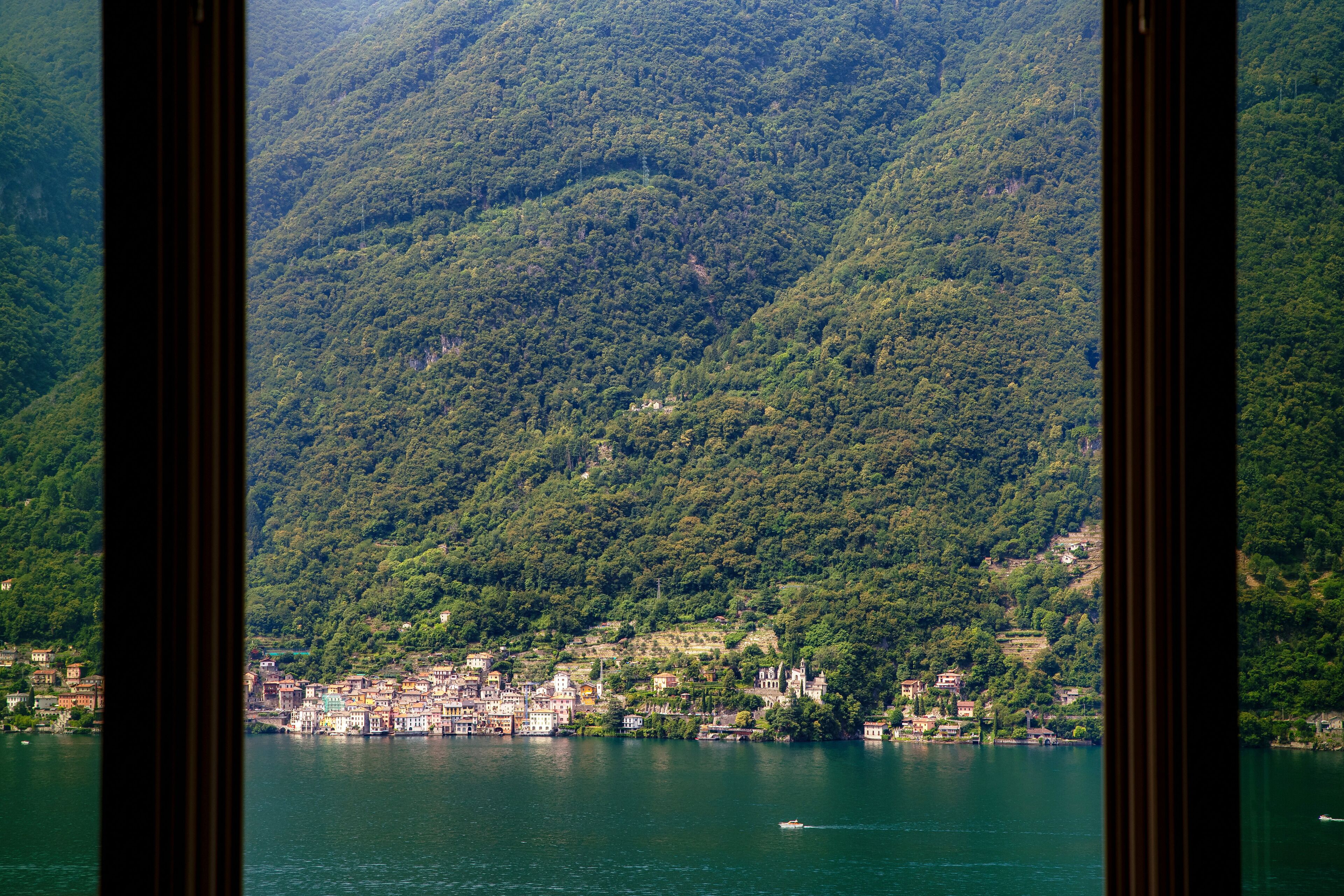 A lake surrounded by lush green hills and a small town with buildings along the shore.