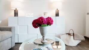 Una sala de estar moderna con una mesa de centro de vidrio, un florero con flores rosas, una revista y un sofá blanco.