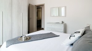 Una habitación de hotel con cama, mesita de noche con lámpara, armario y espejo en la pared.