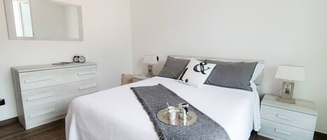 A neatly arranged bedroom with a large bed, a dresser, a nightstand, and a mirror on the wall.