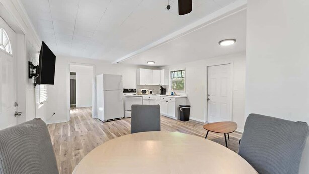 A modern kitchen with white cabinets, a refrigerator, and a sink. There is a dining area with a round table and two chairs. - Cozy Cottage | Fenced Yard & Fire Pit (Homosassa)