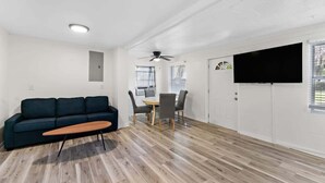 A modern living room with a dark blue sofa, a wooden coffee table, and a dining area with a round table and chairs. - Cozy Cottage | Fenced Yard & Fire Pit (Homosassa)