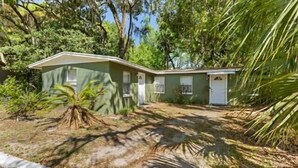 A single-story house with a green exterior, a small porch, and a yard with sparse vegetation. - Cozy Cottage | Fenced Yard & Fire Pit (Homosassa)