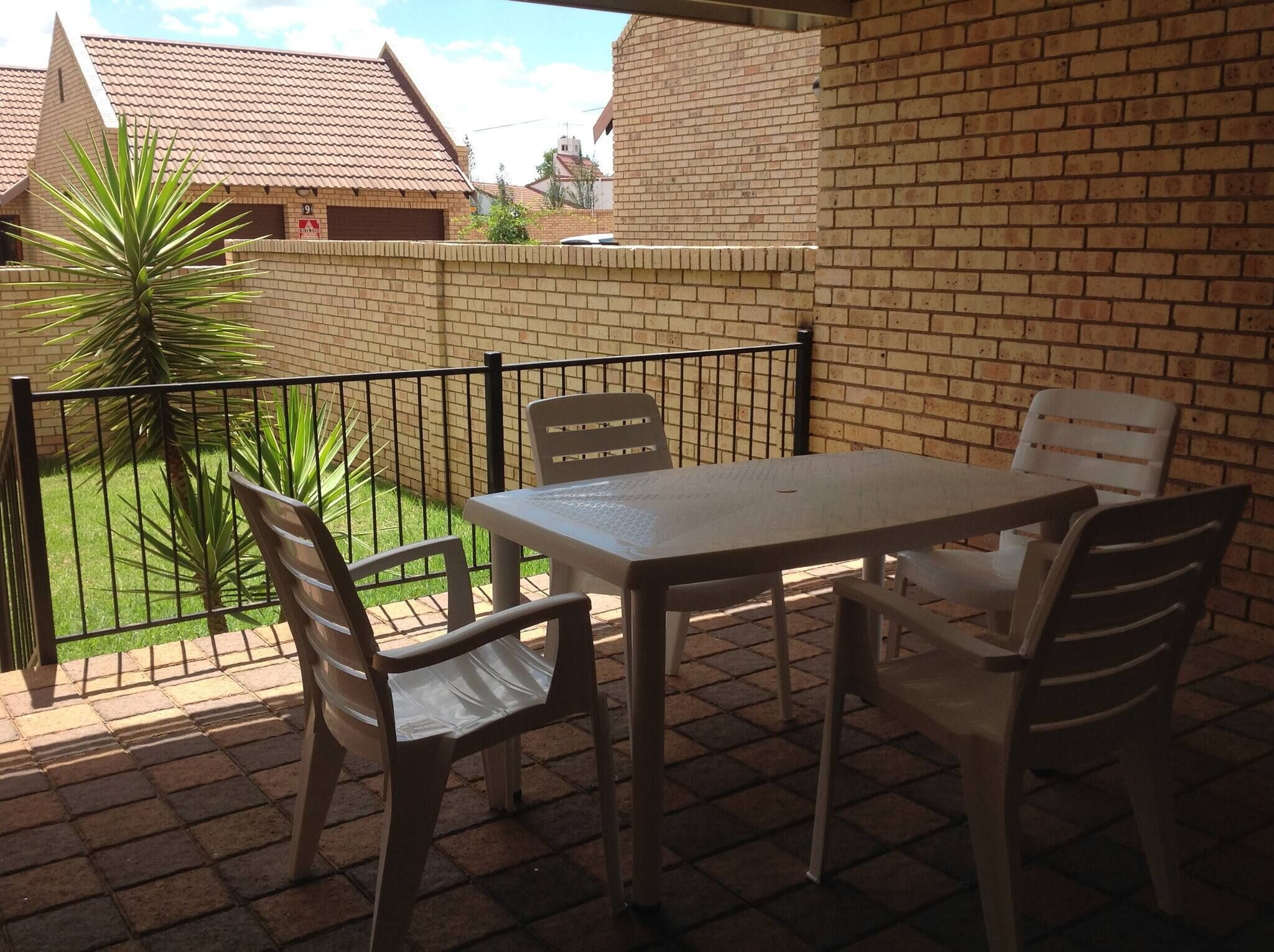 Une terrasse avec une table et des chaises, un mur en briques et une vue sur un quartier résidentiel.