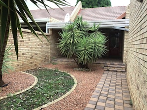 A courtyard with a brick wall, a palm tree, and a small garden area. - Fully Furnished Rentals Bloemfontein (Bloemfontein)