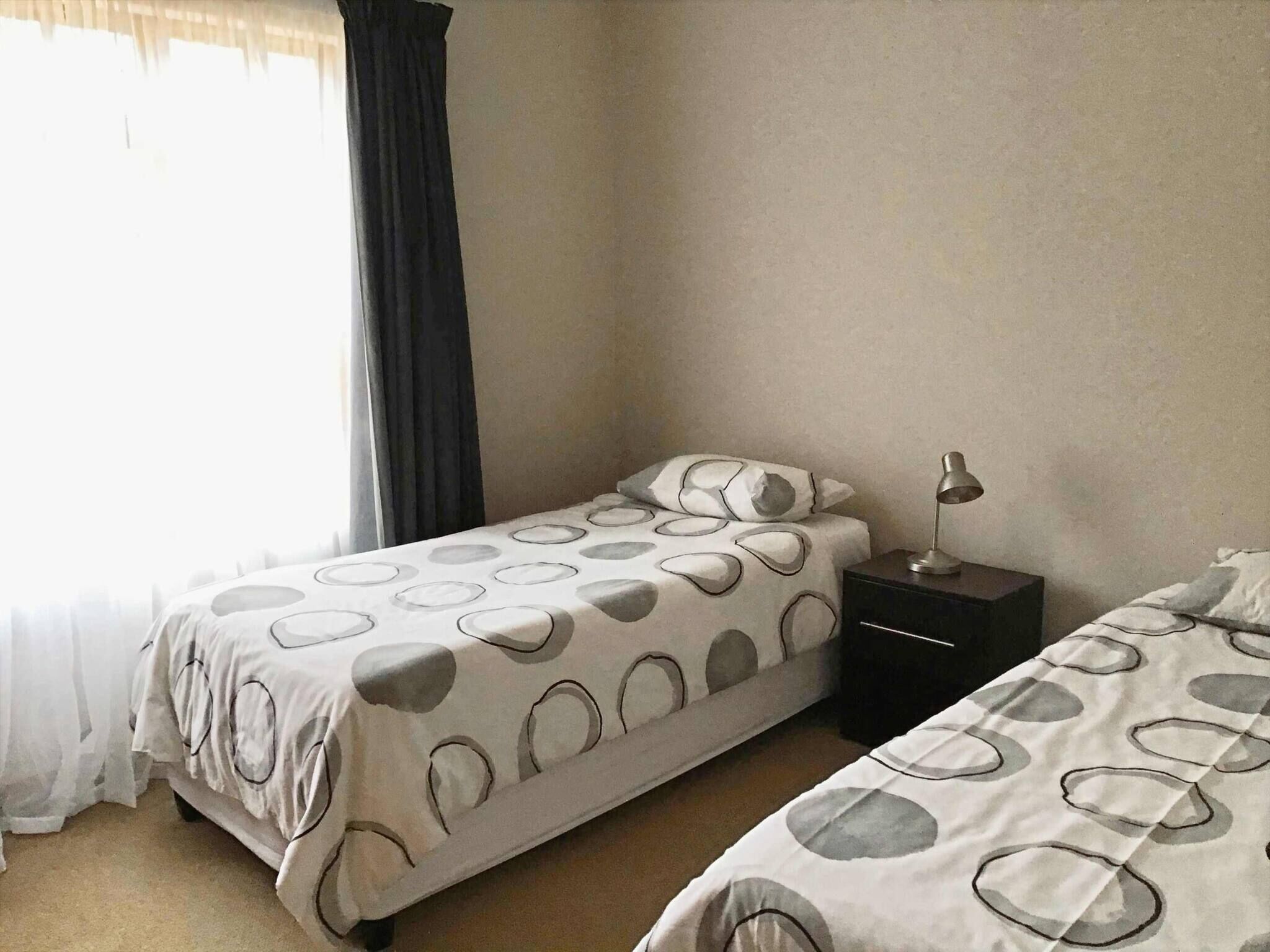 Un dormitorio con dos camas, una mesita de noche, una lámpara y una ventana con cortinas.